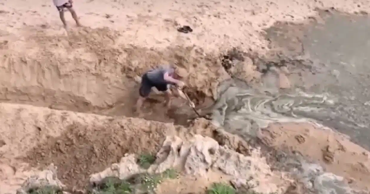 Pessoa escavando na areia com água corrente.